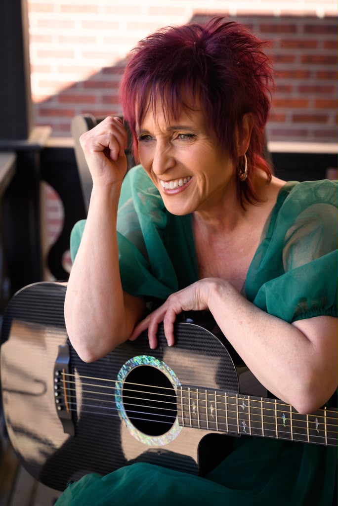 Randie O’Neil seated outdoors with her guitar